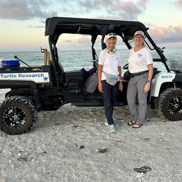 two women standing on beach in front of ATV
