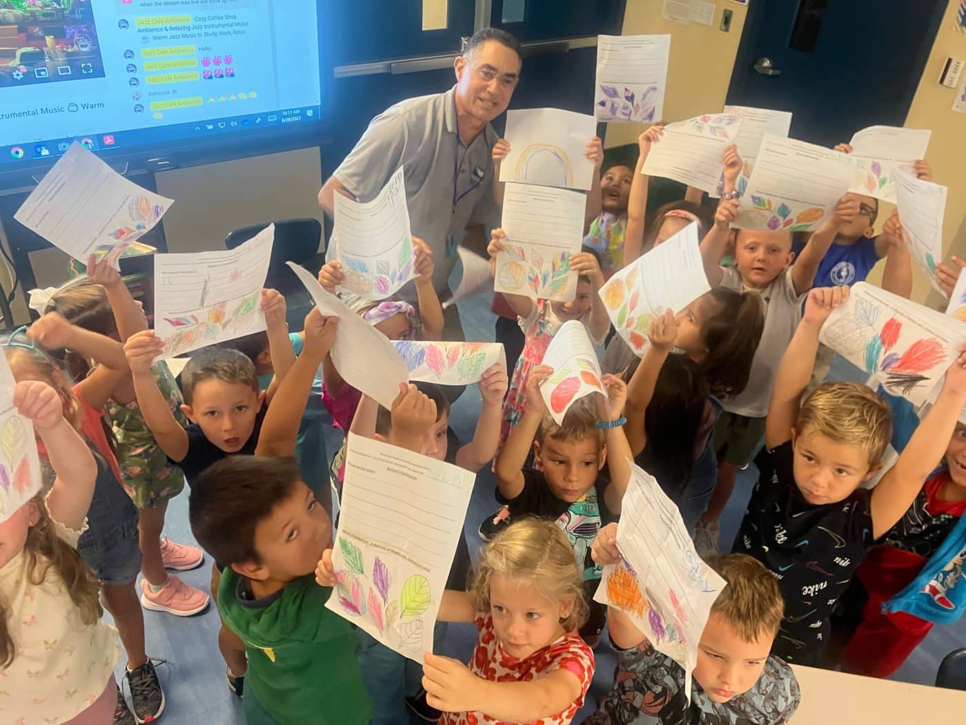 class of Sanibel School children holding up colorful sheets of paper next to SCCF Environmental Educator Richard Finkel