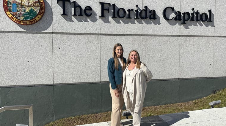 two women in front of outdoor sign that says 'the florida capitol'