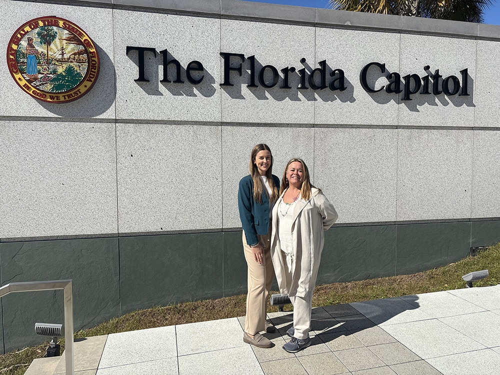 two women in front of outdoor sign that says 'the florida capitol'