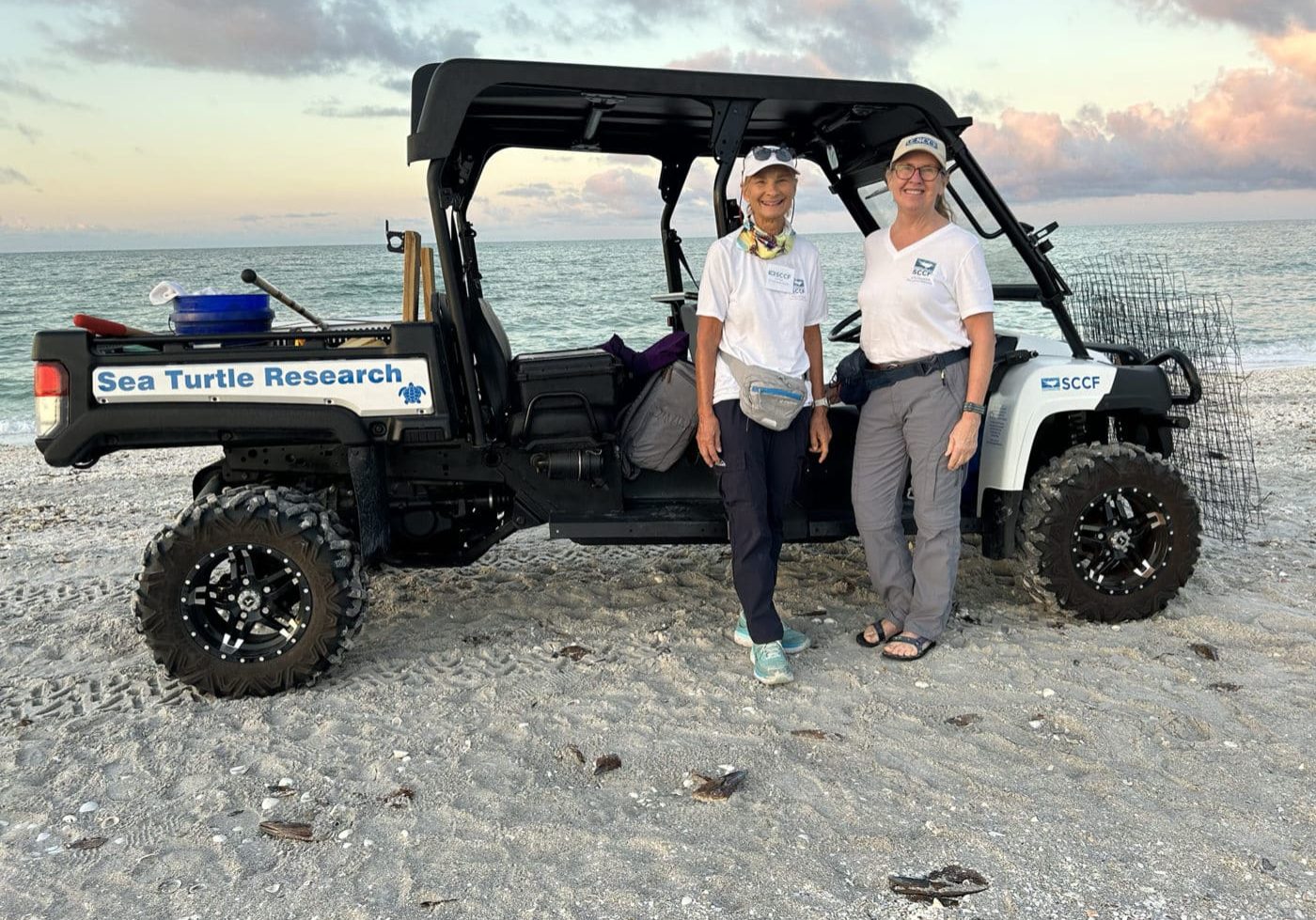 two women standing on beach in front of ATV